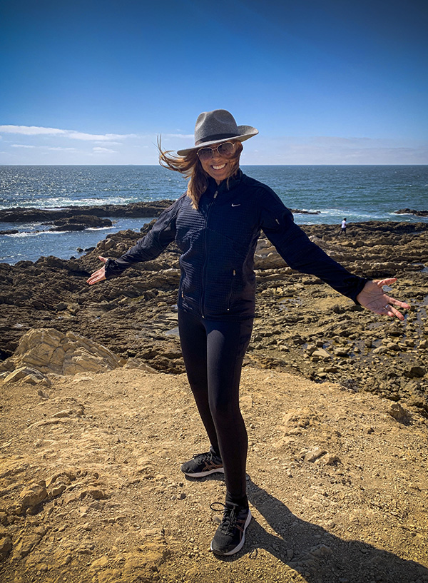 A woman in black pants and a hat standing on the beach.